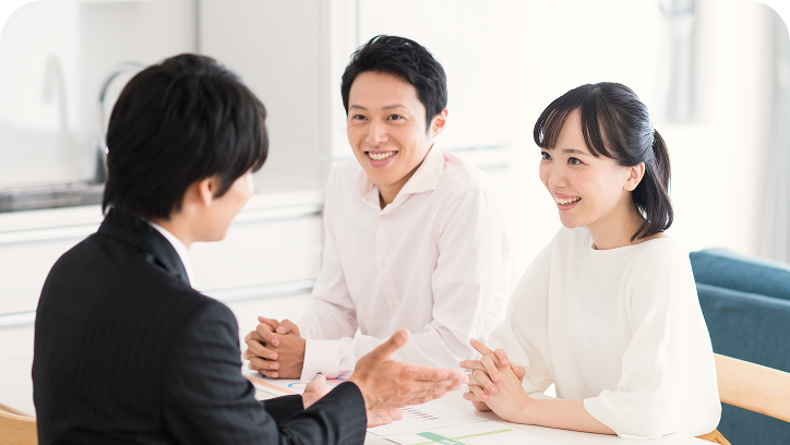 保険相談の場面。スーツの男性アドバイザーにと笑顔で話を聞くカップルの様子