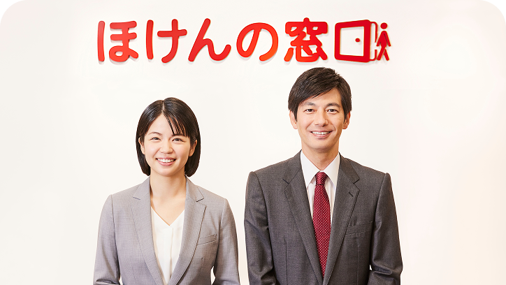 『ほけんの窓口』のロゴの前に立つスーツ姿の男女スタッフ。笑顔で並んでいる様子